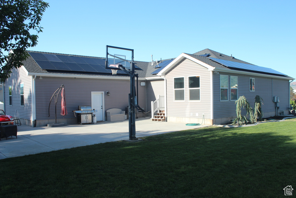 Back of house featuring solar panels, entry steps, a lawn, and a shingled roof