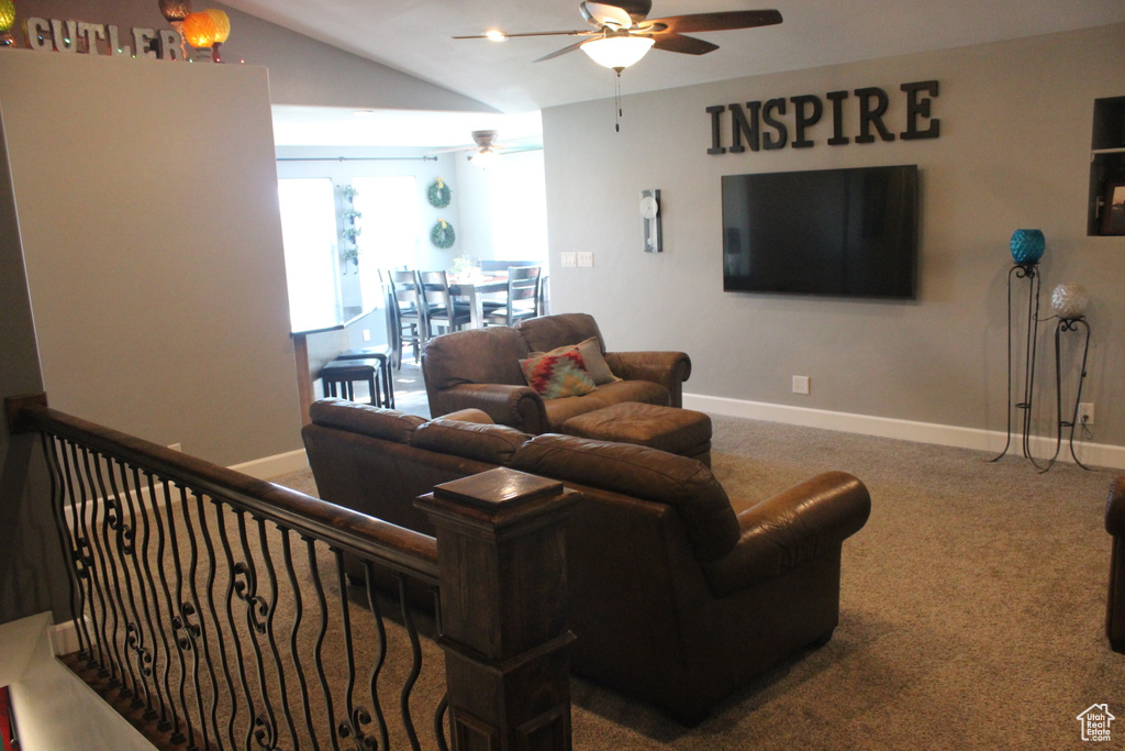 Carpeted living room featuring ceiling fan, baseboards, and vaulted ceiling