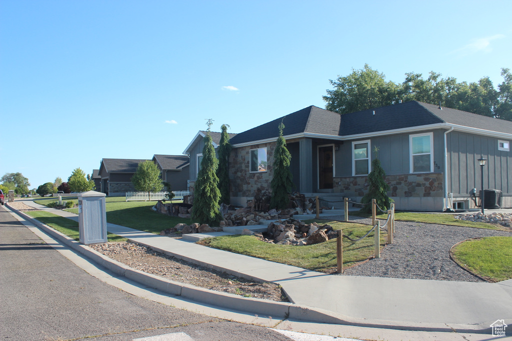Ranch-style home featuring board and batten siding, stone siding, and a front lawn