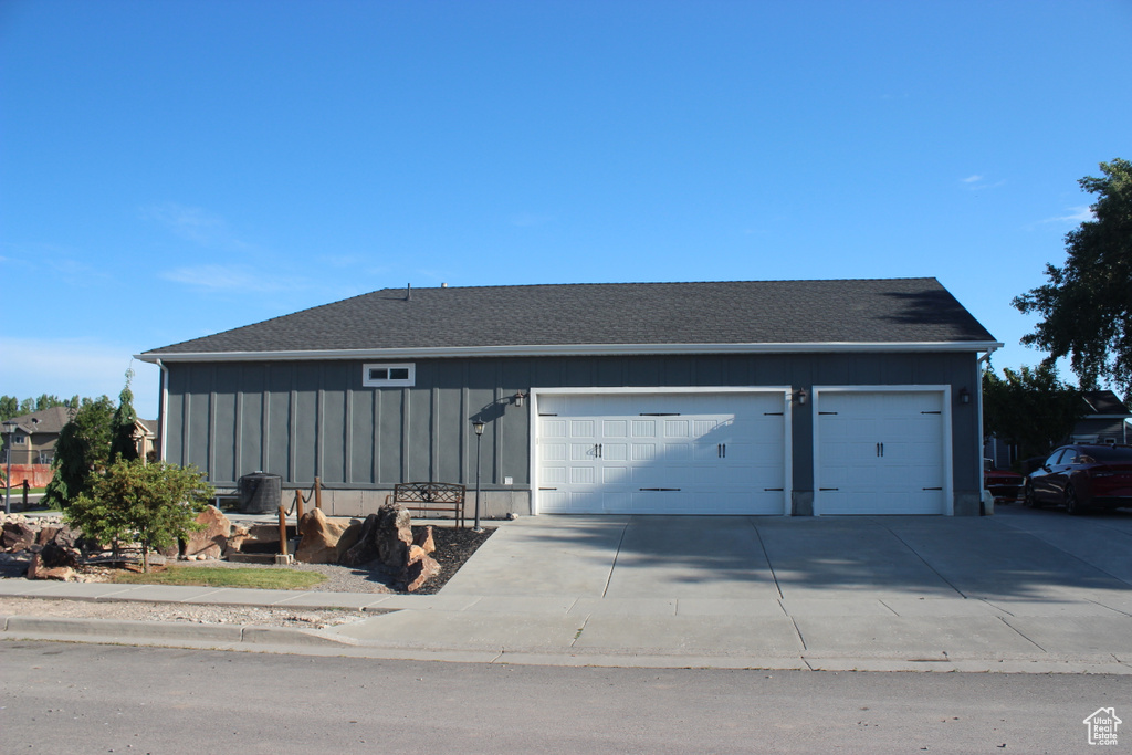 Ranch-style home with an attached garage, concrete driveway, board and batten siding, and a shingled roof