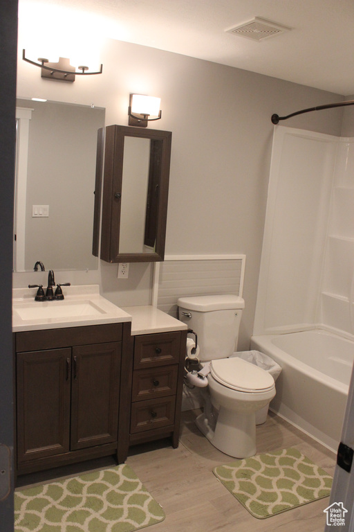 Full bath featuring toilet, vanity, wood finished floors, and washtub / shower combination