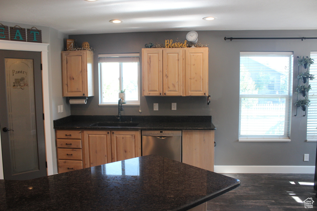 Kitchen with stainless steel dishwasher, a sink, light brown cabinetry, dark wood-style floors, and baseboards