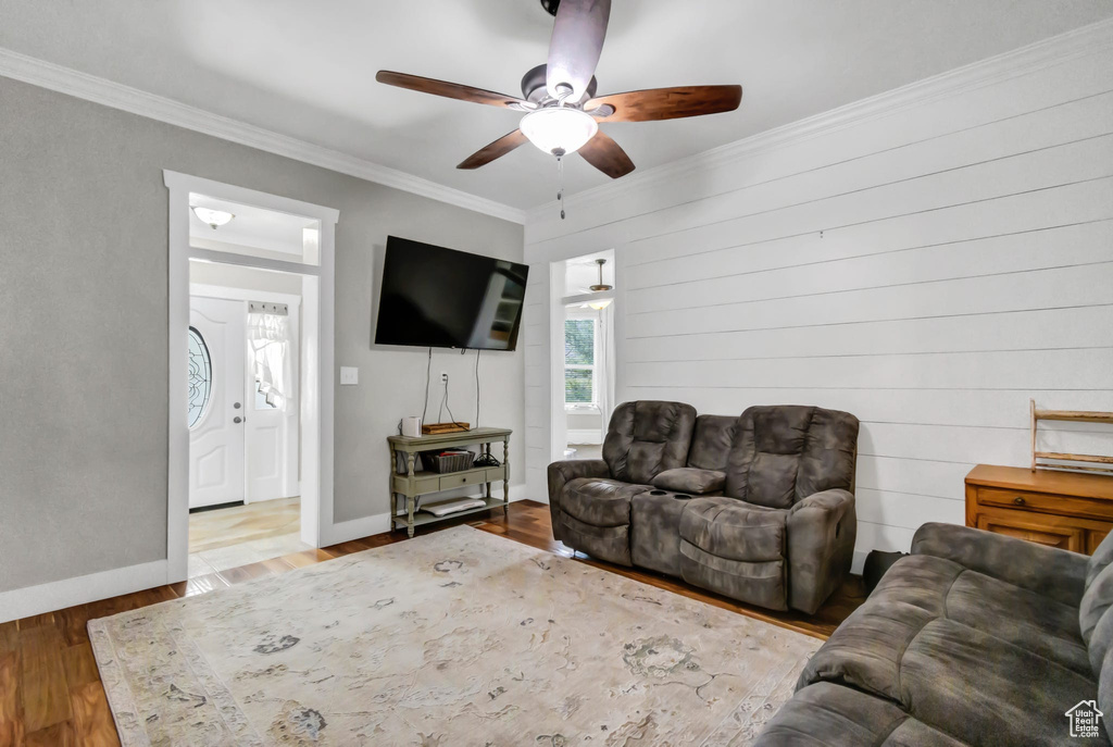 Living room featuring a ceiling fan, wood finished floors, crown molding, and baseboards