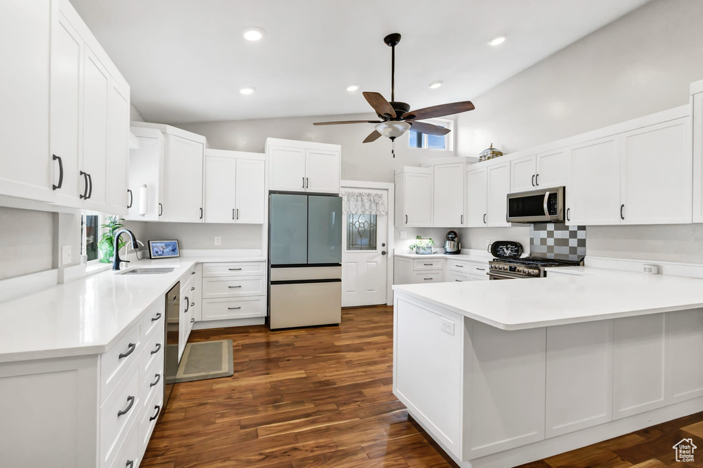 Kitchen featuring appliances with stainless steel finishes, a sink, ceiling fan, a peninsula, and high vaulted ceiling