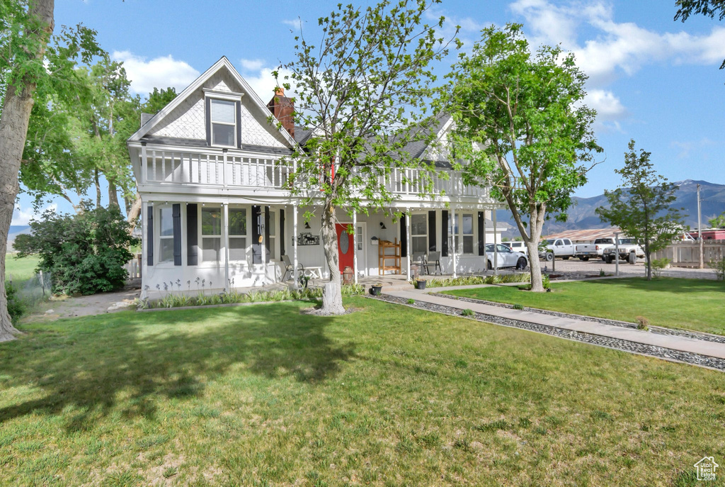 Victorian home with a front yard, a porch, a chimney, and a balcony