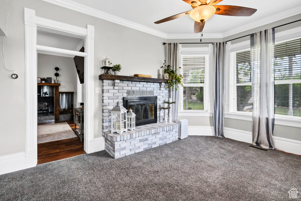 Unfurnished living room with a brick fireplace, carpet, crown molding, a ceiling fan, and baseboards