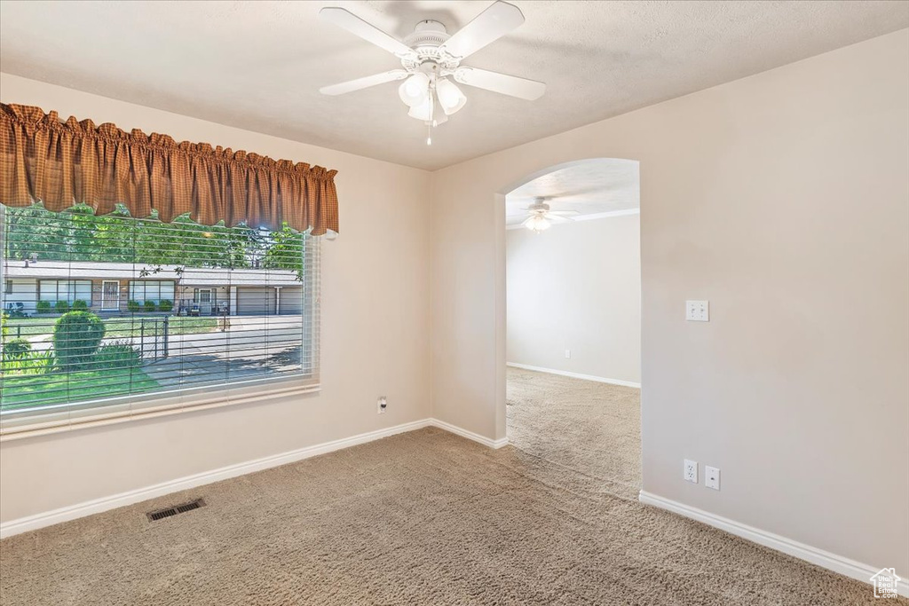 Carpeted empty room featuring ceiling fan, arched walkways, and baseboards