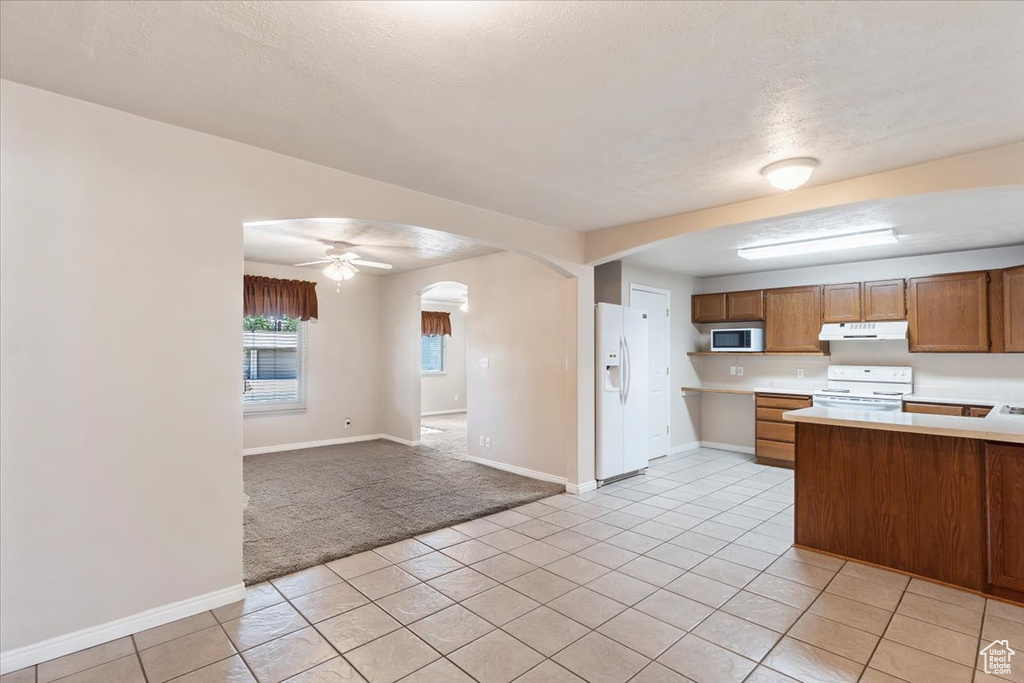 Kitchen featuring white appliances, arched walkways, light countertops, under cabinet range hood, and baseboards