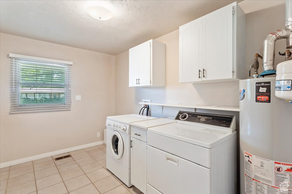 Laundry room featuring gas water heater, washer and dryer, cabinet space, baseboards, and a textured ceiling