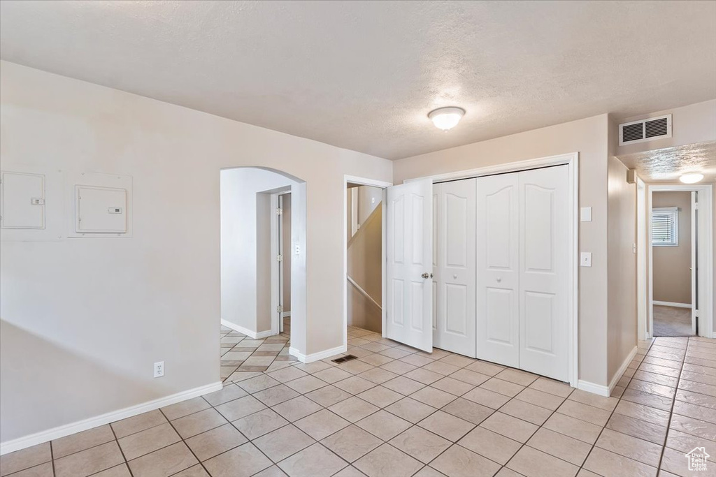 Unfurnished bedroom with arched walkways, light tile patterned floors, a closet, a textured ceiling, and baseboards