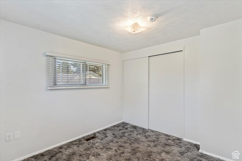Unfurnished bedroom featuring carpet floors, baseboards, a closet, and a textured ceiling