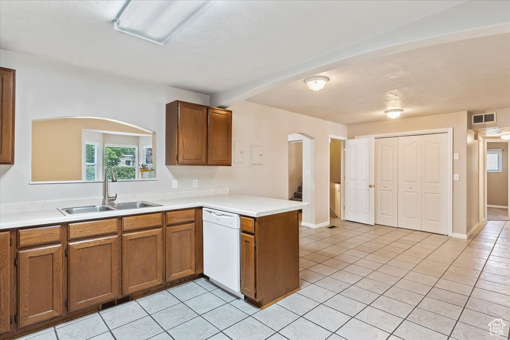 Kitchen featuring dishwasher, a sink, arched walkways, brown cabinets, and a peninsula
