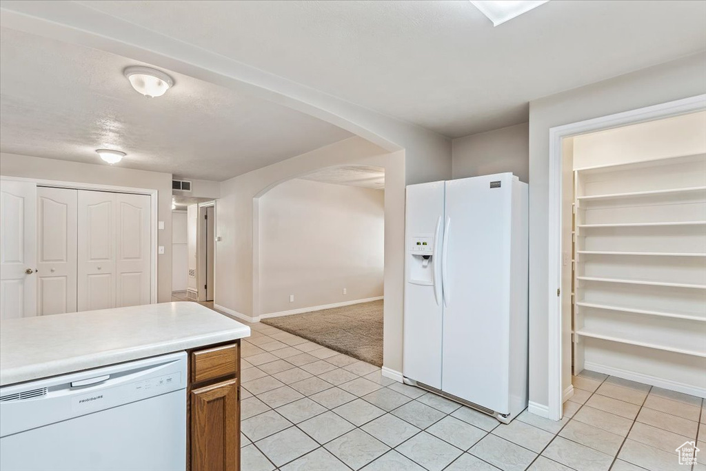 Kitchen with white appliances, light tile patterned floors, arched walkways, light countertops, and baseboards