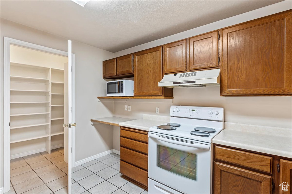 Kitchen featuring under cabinet range hood, white appliances, light tile patterned floors, light countertops, and brown cabinetry