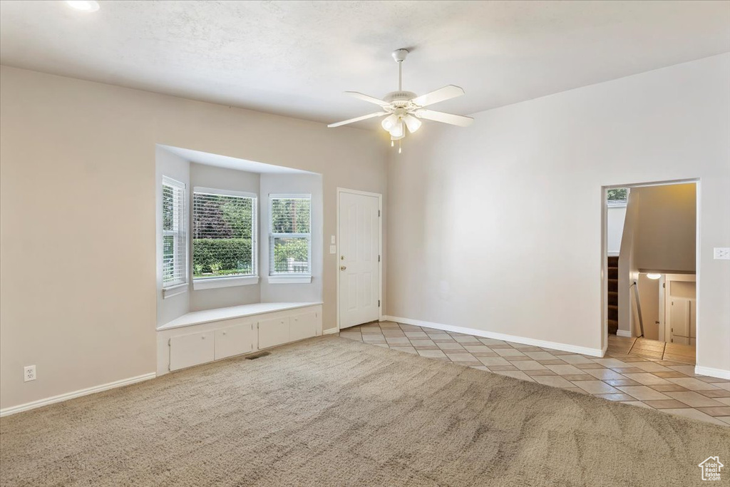 Empty room with a ceiling fan, light tile patterned flooring, baseboards, and light carpet
