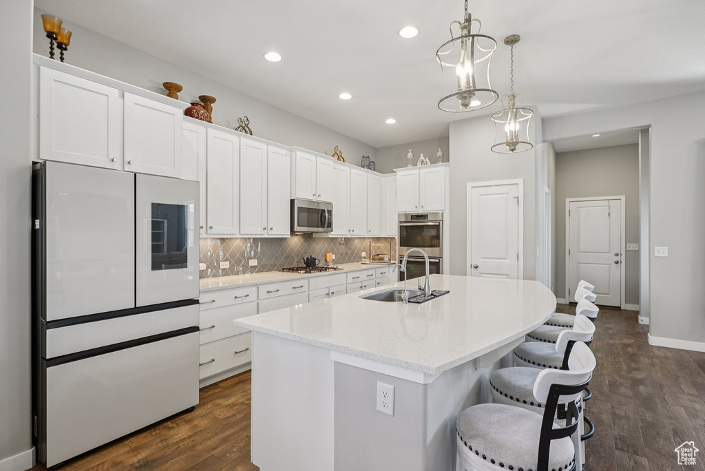 Kitchen with stainless steel appliances, a sink, white cabinets, recessed lighting, and an island with sink