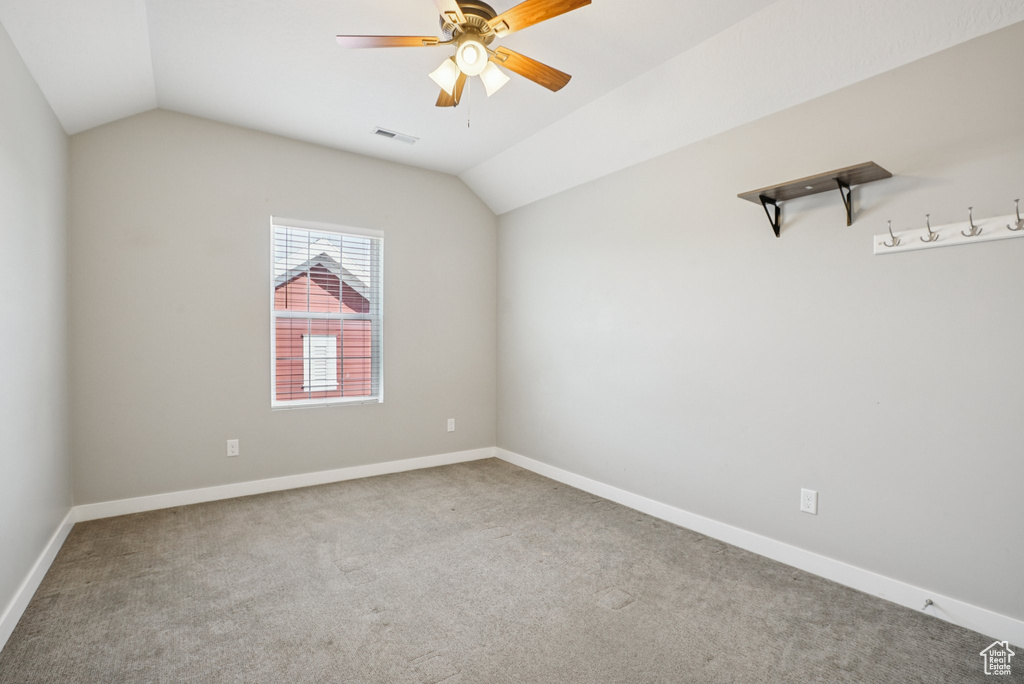 Empty room featuring vaulted ceiling, a ceiling fan, carpet, and baseboards