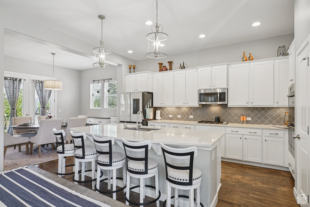 Kitchen with a sink, stainless steel appliances, light countertops, a center island with sink, and decorative backsplash