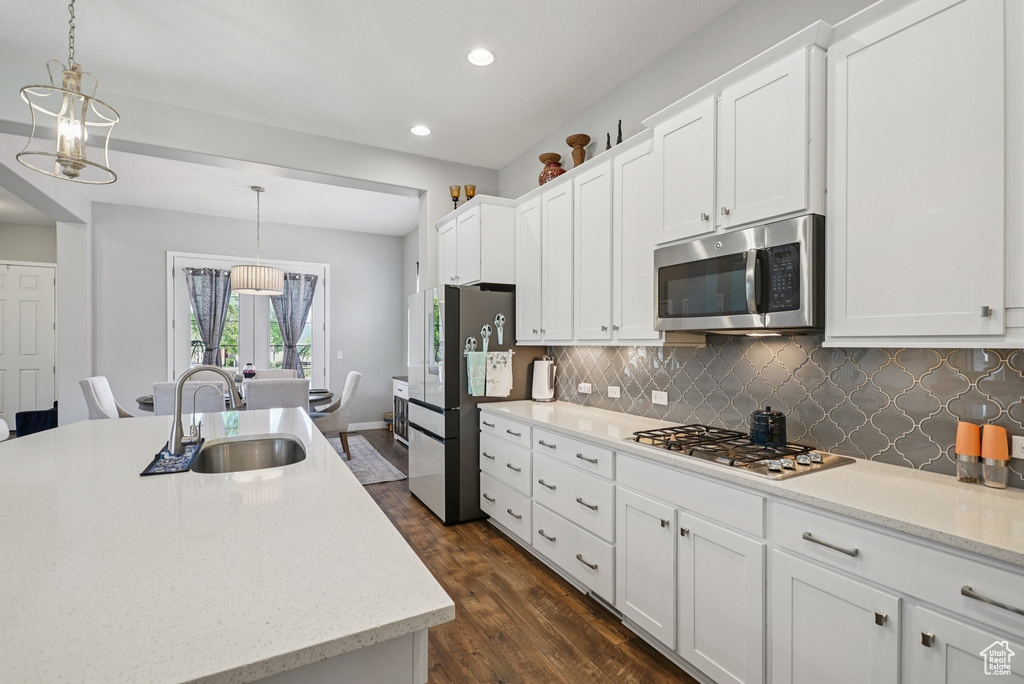 Kitchen with appliances with stainless steel finishes, a sink, dark wood-style floors, backsplash, and white cabinetry
