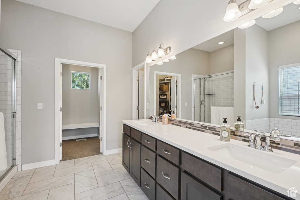 Bathroom with a walk in closet, a stall shower, double vanity, baseboards, and marble look tiles