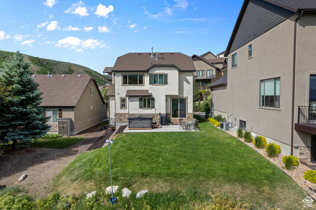 Back of house with a patio area, a hot tub, a residential view, stucco siding, and a lawn