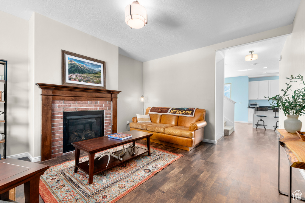 Living area with dark wood finished floors, baseboards, a fireplace, and a textured ceiling