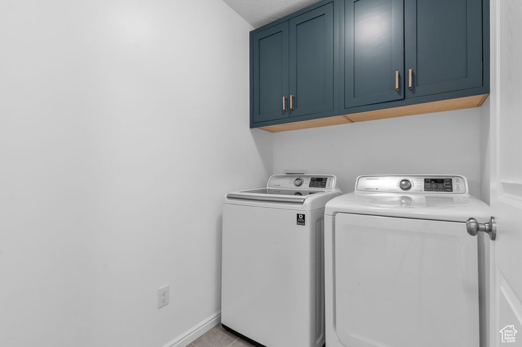 Washroom featuring cabinet space, washing machine and dryer, and light tile patterned floors