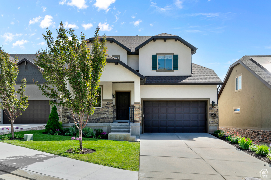 View of front of property with stucco siding, stone siding, a garage, a front yard, and concrete driveway