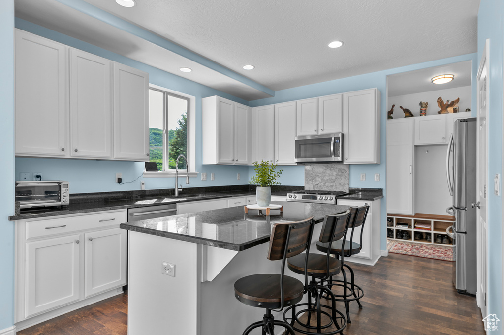 Kitchen featuring appliances with stainless steel finishes, dark wood finished floors, a center island, white cabinetry, and recessed lighting