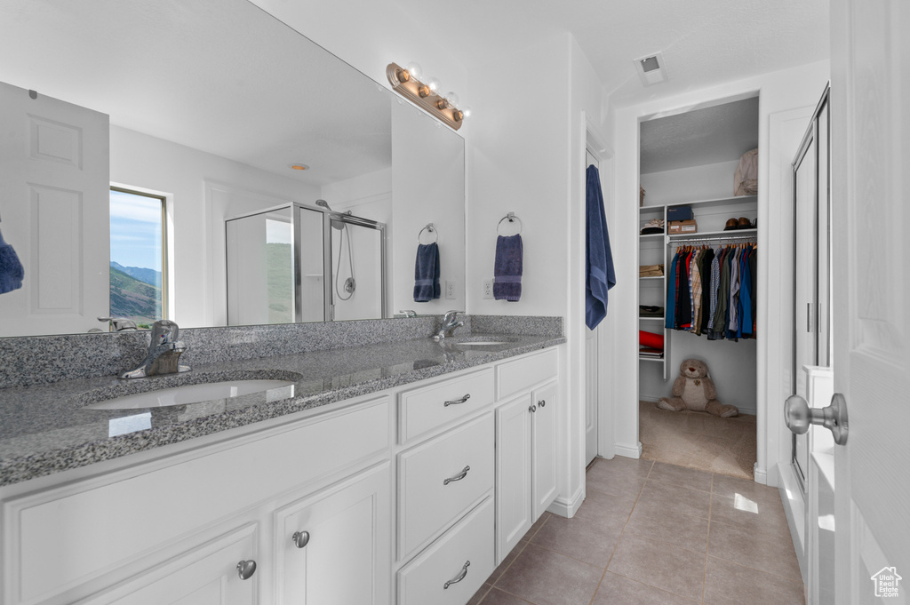 Full bathroom with a stall shower, double vanity, a spacious closet, and tile patterned floors