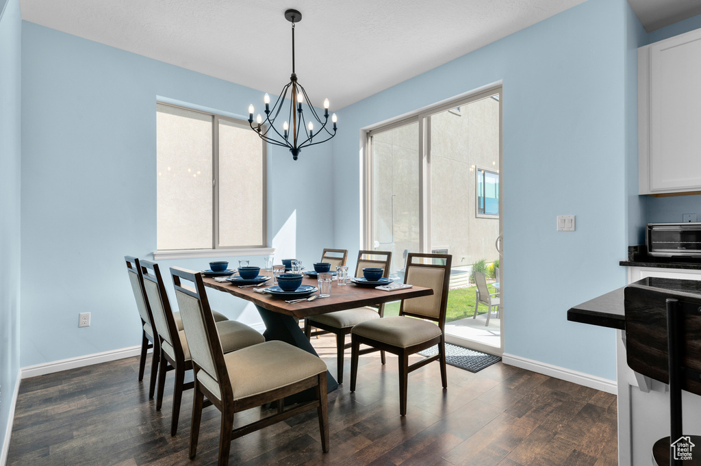 Dining room featuring dark wood-style flooring, a chandelier, and baseboards