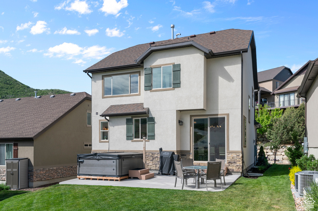 Back of house featuring a hot tub, a patio, cooling unit, and stucco siding