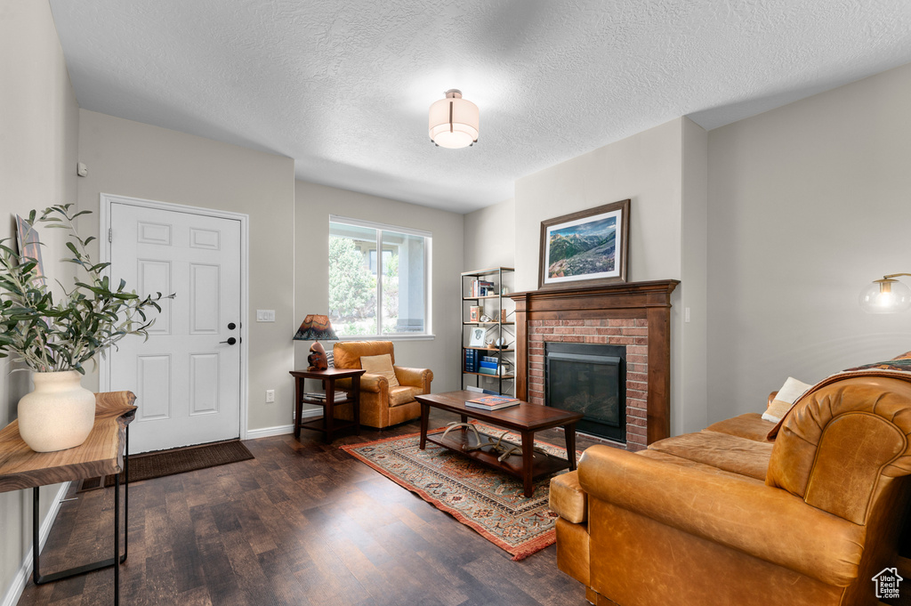 Living area with wood finished floors, a textured ceiling, a brick fireplace, and baseboards