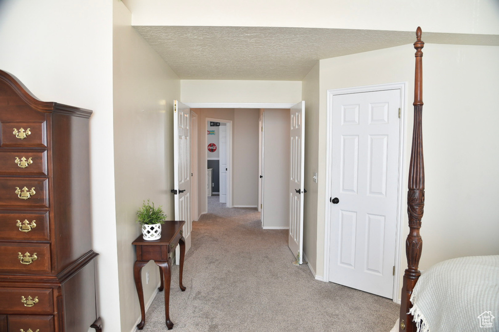 Hallway with light colored carpet, a textured ceiling, and baseboards