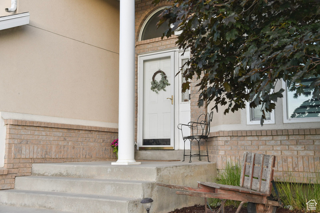 Doorway to property featuring stucco siding, brick siding, stone siding, and covered porch