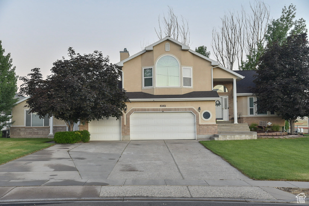 View of front of house featuring an attached garage, driveway, a front lawn, and stucco siding