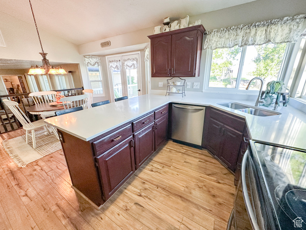 Kitchen with appliances with stainless steel finishes, a sink, light countertops, light wood finished floors, and lofted ceiling