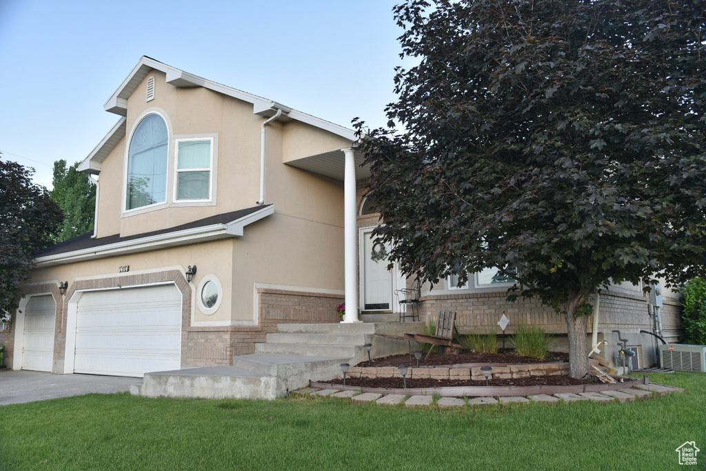 View of front facade featuring brick siding, a garage, stucco siding, a front yard, and driveway