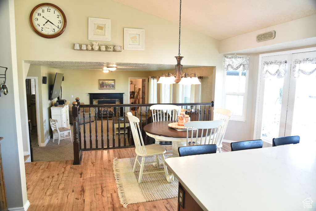 Dining room featuring vaulted ceiling, light wood-style floors, a chandelier, a fireplace, and baseboards