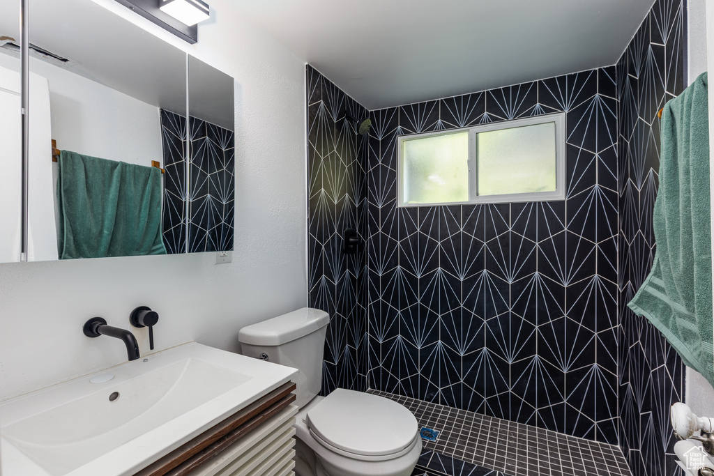 Bathroom featuring toilet, tiled shower, and vanity