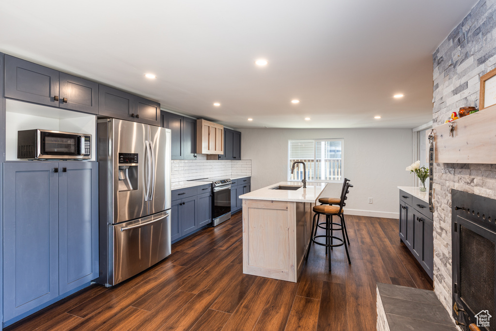 Kitchen featuring appliances with stainless steel finishes, a sink, light countertops, decorative backsplash, and a breakfast bar area