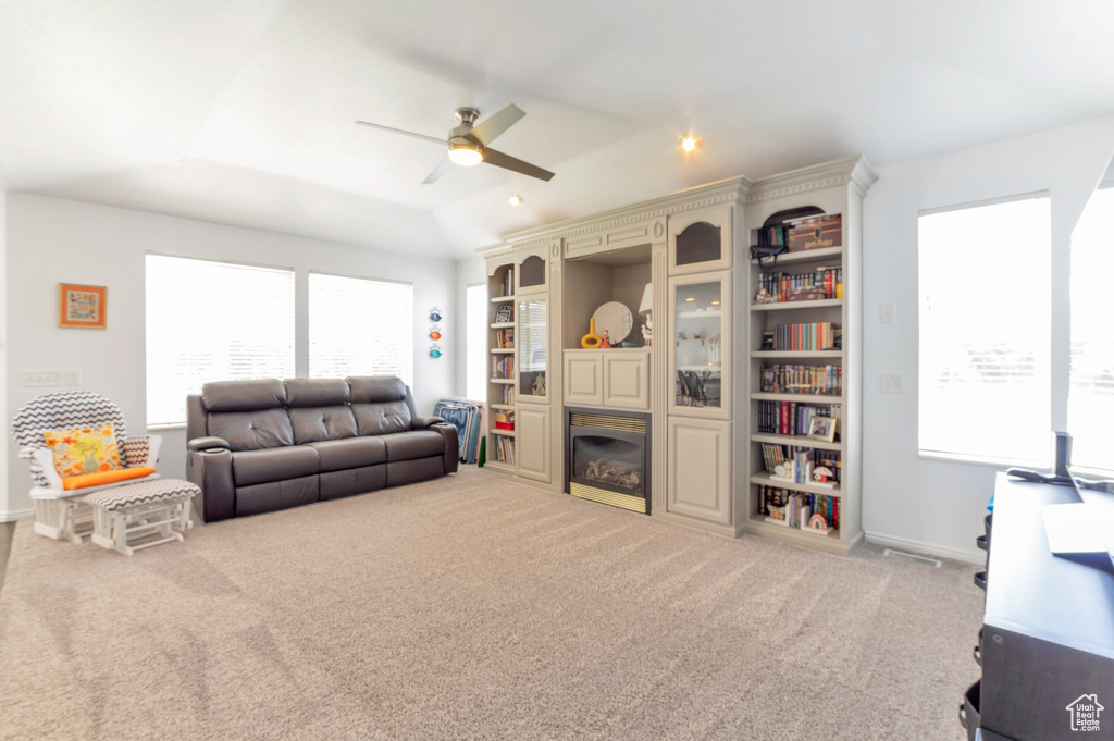 Living room featuring ceiling fan, a glass covered fireplace, carpet, and healthy amount of natural light