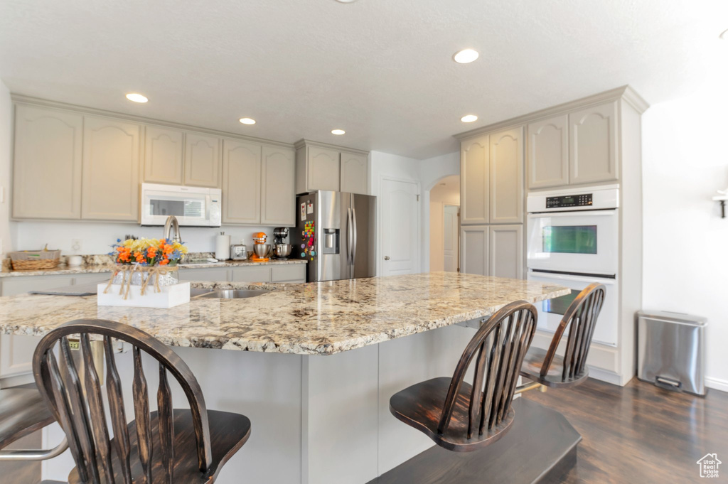 Kitchen with white appliances, recessed lighting, arched walkways, a breakfast bar, and dark wood-style flooring