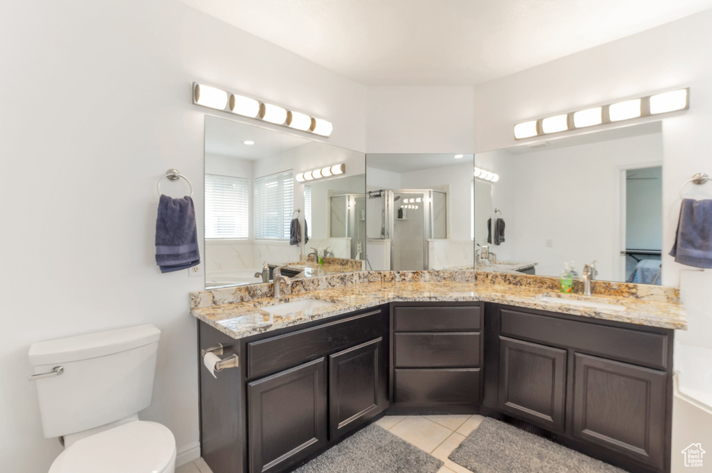 Bathroom featuring a stall shower, double vanity, tile patterned floors, toilet, and a garden tub