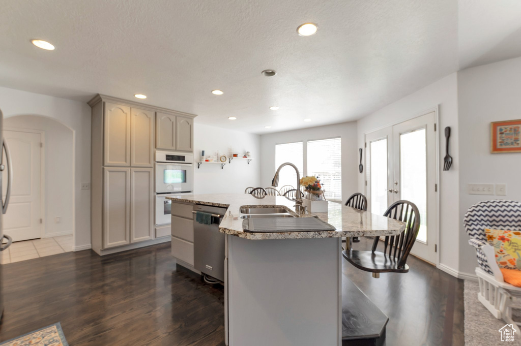 Kitchen featuring stainless steel dishwasher, white double oven, a sink, a breakfast bar, and dark wood-style flooring