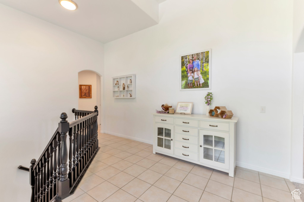 Hall featuring an upstairs landing, light tile patterned flooring, baseboards, and arched walkways