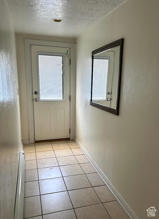 Doorway to outside featuring baseboard heating, light tile patterned flooring, a textured ceiling, and baseboards