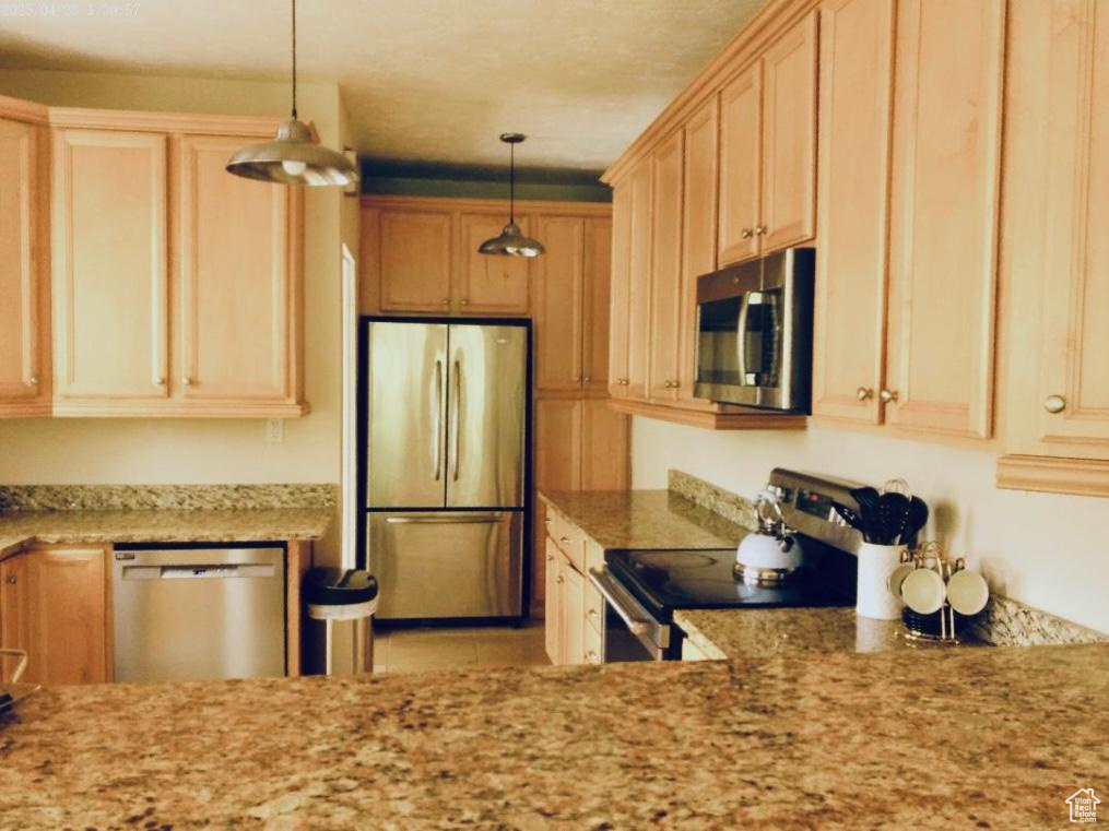 Kitchen featuring appliances with stainless steel finishes, pendant lighting, light stone countertops, and light brown cabinetry