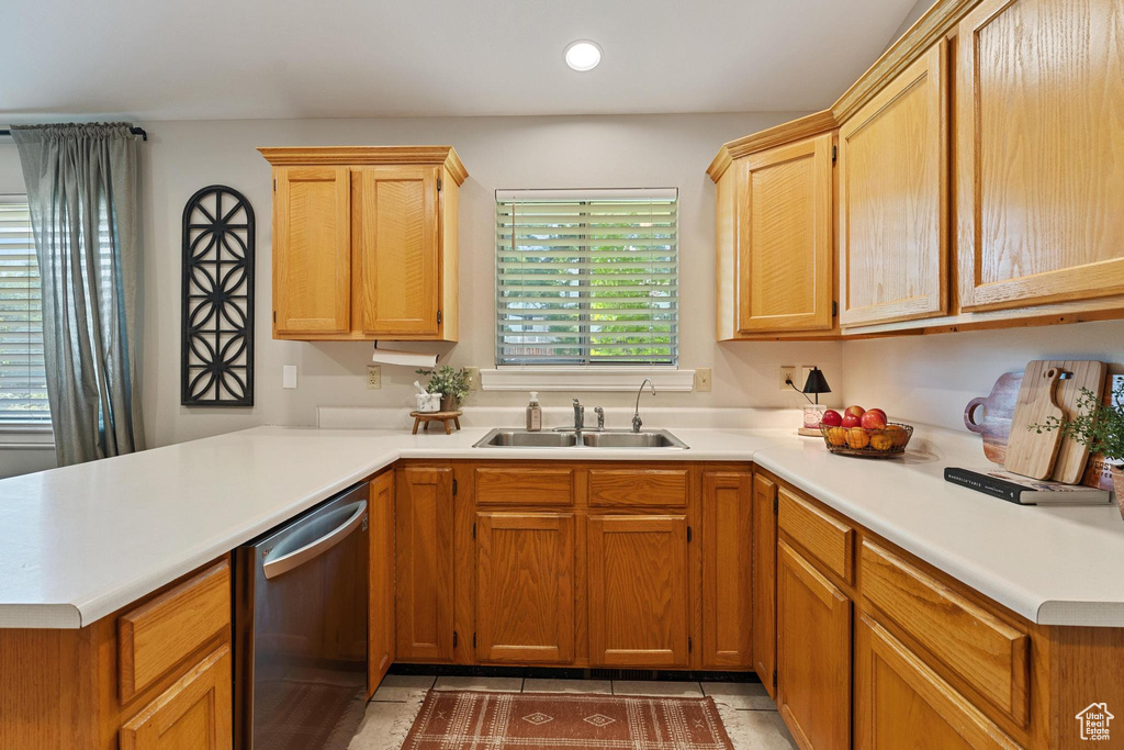 Kitchen with stainless steel dishwasher, a sink, light countertops, a peninsula, and light tile patterned floors