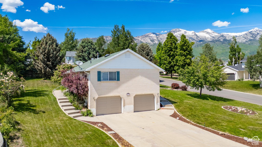 View of home's exterior featuring concrete driveway, an attached garage, a lawn, a mountain view, and stairs